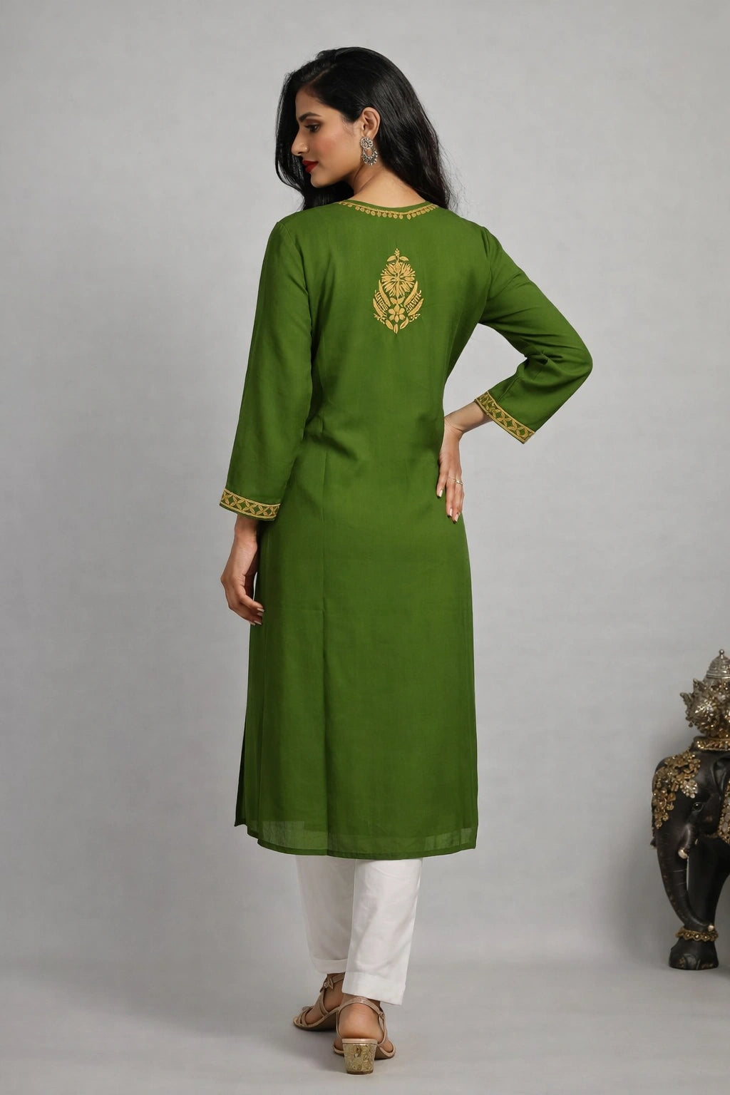Woman wearing a lucknowi chikankari green kurta with white pants on a gray background