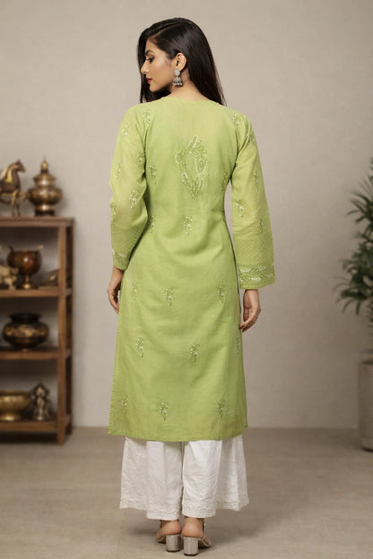Woman wearing a green embroidered kurta with white pants in a neutral setting.