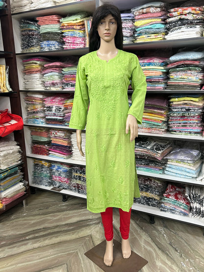 A mannequin wearing a bright lime green embroidered kurta with three-quarter sleeves and red leggings, standing in front of shelves filled with folded clothing in a retail store.