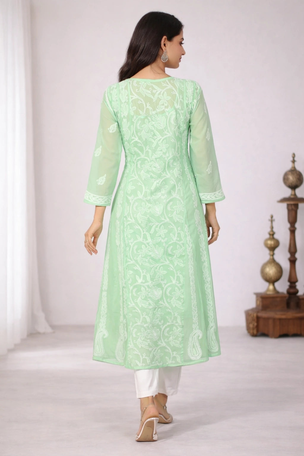 Woman wearing a light green embroidered kurta with white pants on a plain background