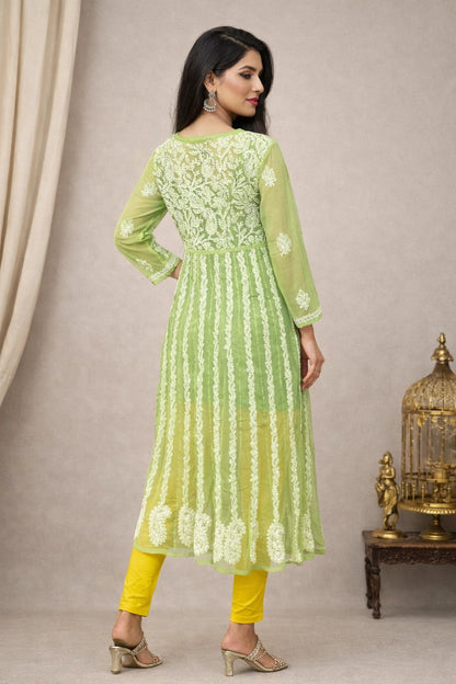 Woman wearing a green and yellow traditional outfit with floral patterns against a beige background.