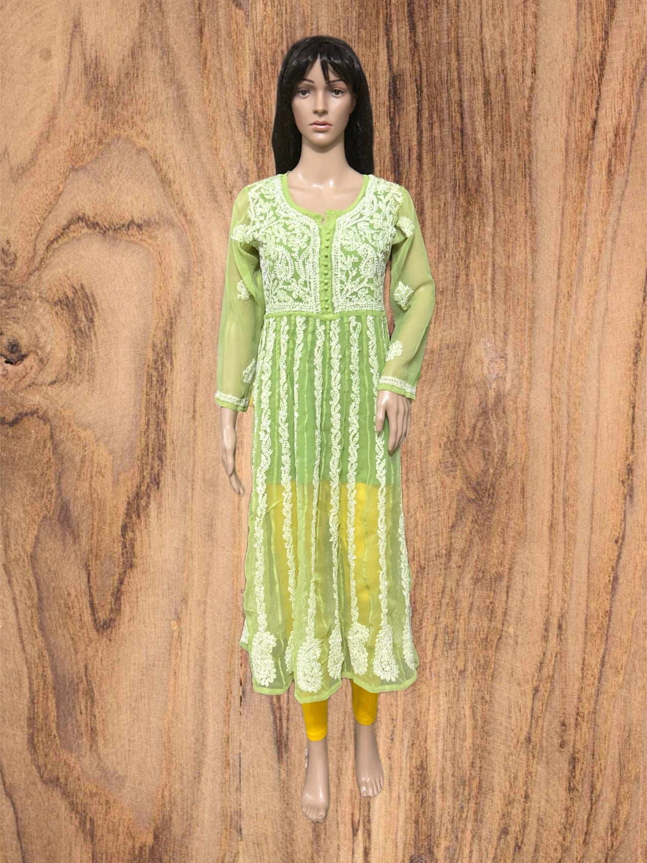Mannequin wearing a green dress with floral patterns against a wooden background