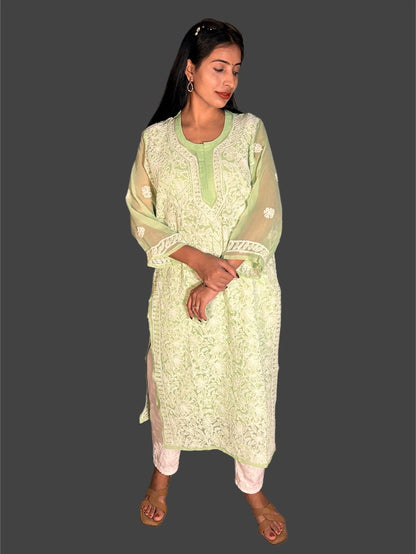 A woman modeling a light green and white embroidered kurta set with sheer sleeves, paired with white pants, against a solid dark gray background.