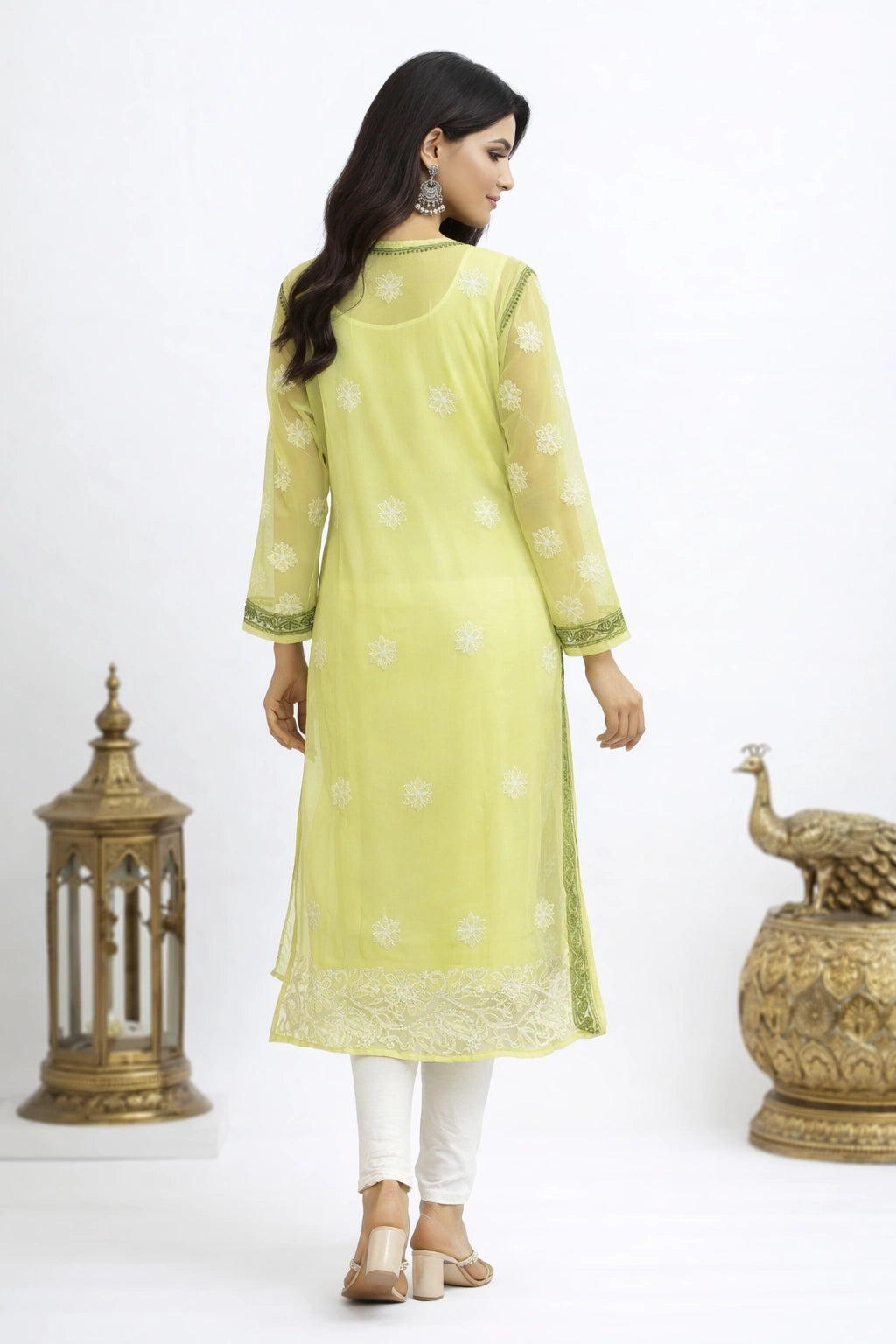 Woman wearing a lucknowi chikankari light green kurta with white patterns, standing between two decorative items on a white background.