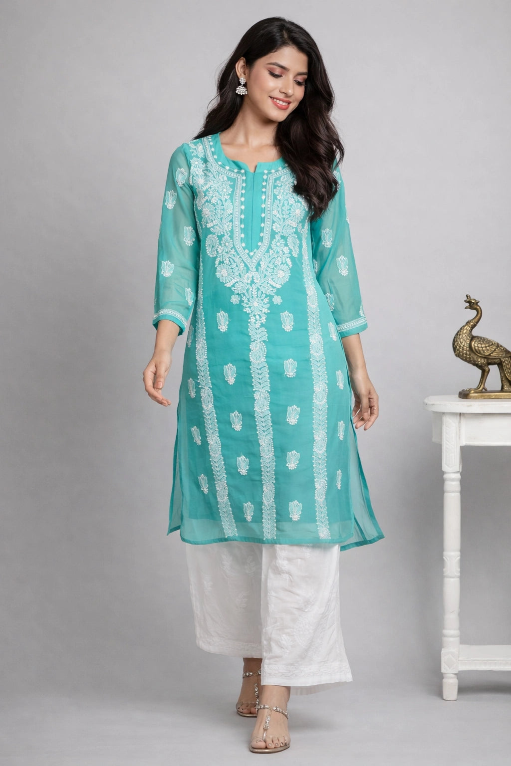 Woman wearing a lucknowi chikankari teal embroidered kurta with white pants against a gray background