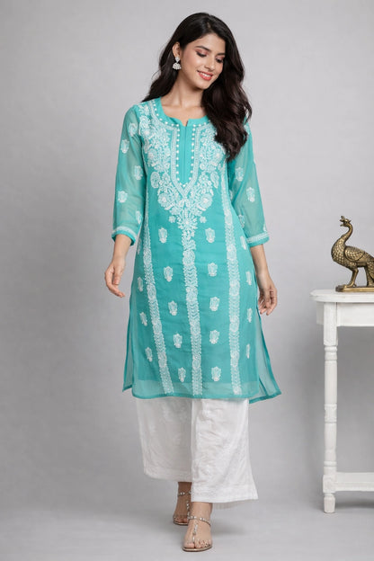 Woman wearing a lucknowi chikankari teal embroidered kurta with white pants against a gray background
