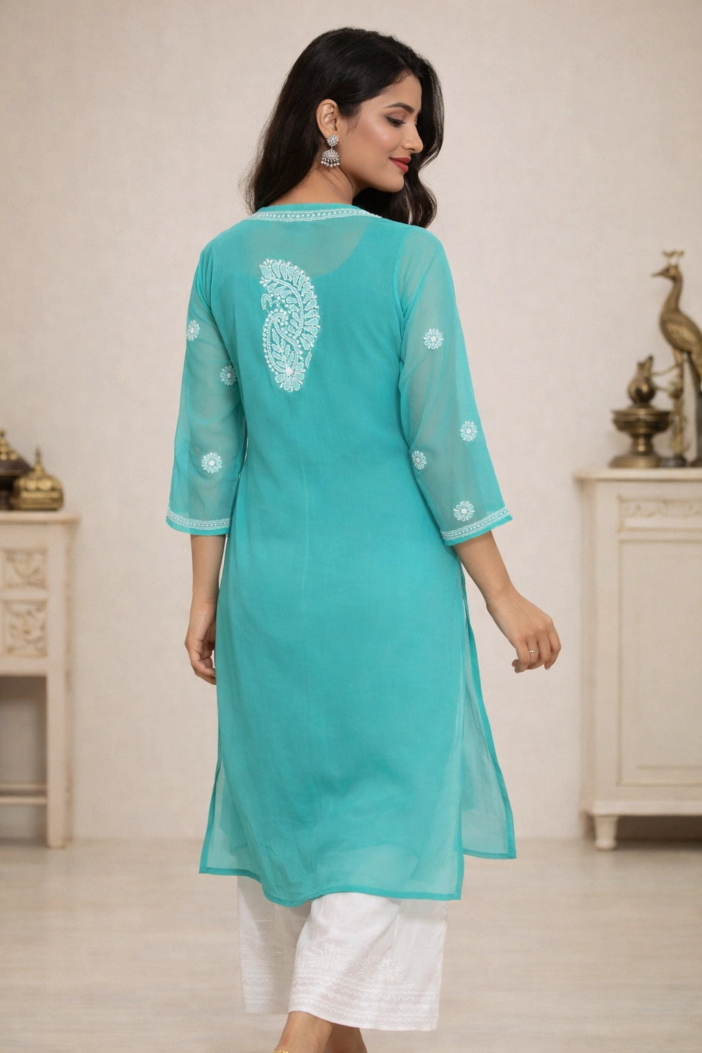 Woman wearing a turquoise kurta with white embroidery in a minimal indoor setting.
