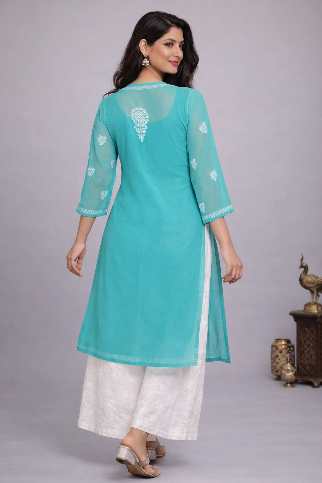 Woman wearing a turquoise kurta with white pants on a gray background