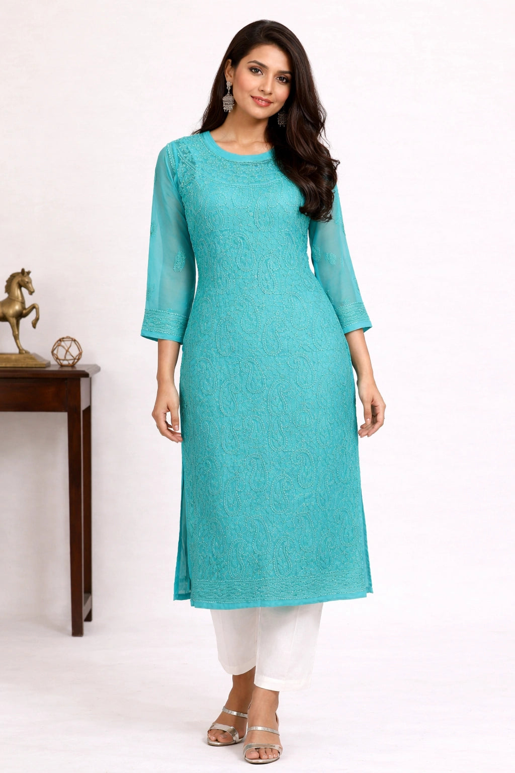 Woman wearing a turquoise kurta with white pants on a plain background