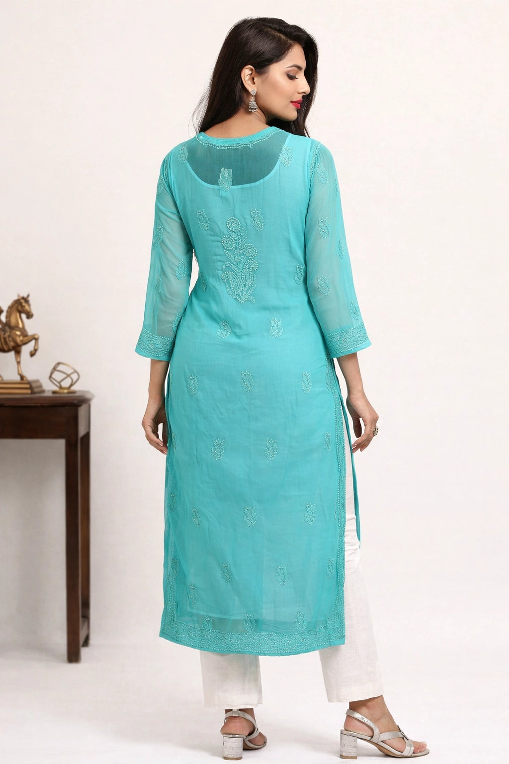 Woman wearing a turquoise kurta with white pants on a plain background