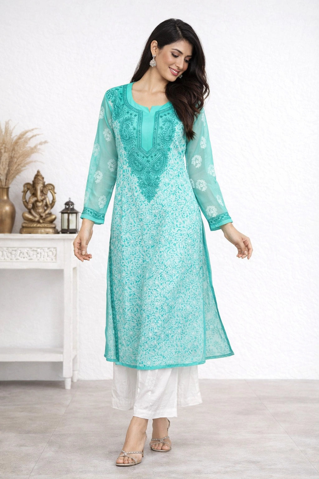 Woman wearing a turquoise embroidered kurta with white pants in a minimalistic room.