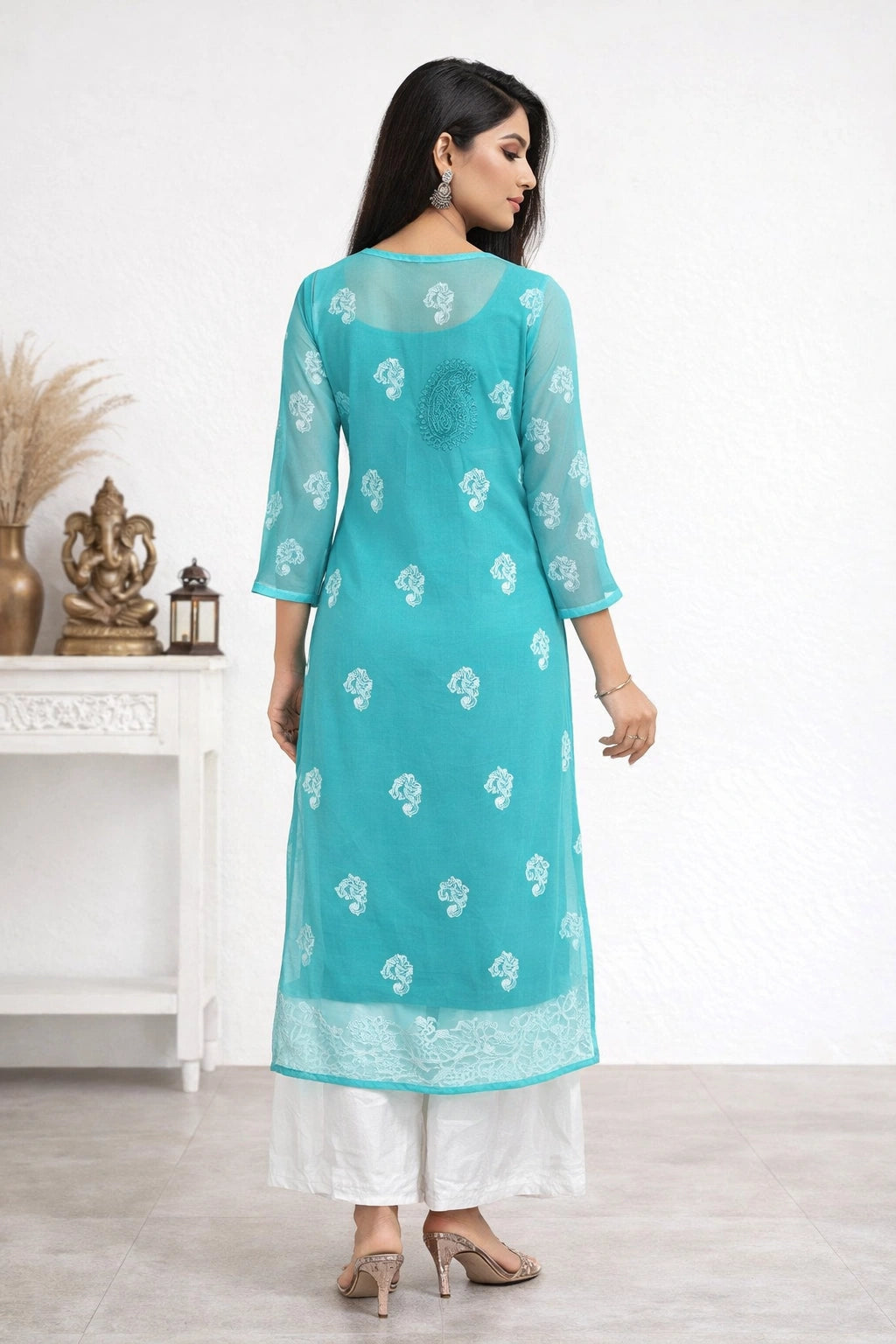 Woman wearing a turquoise embroidered kurta with white pants in a minimalistic setting.