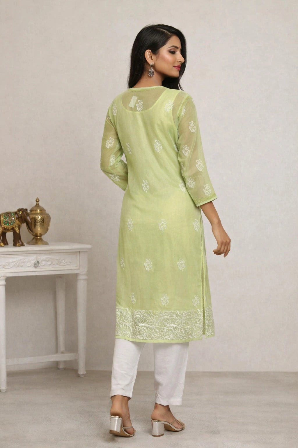 Woman wearing a light green kurta with white floral patterns and white pants, standing in a minimalistic room.