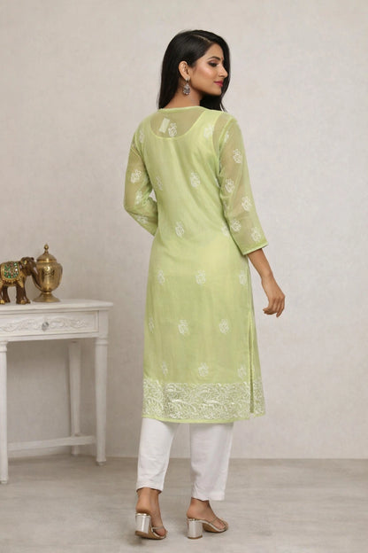 Woman wearing a light green kurta with white floral patterns and white pants, standing in a minimalistic room.
