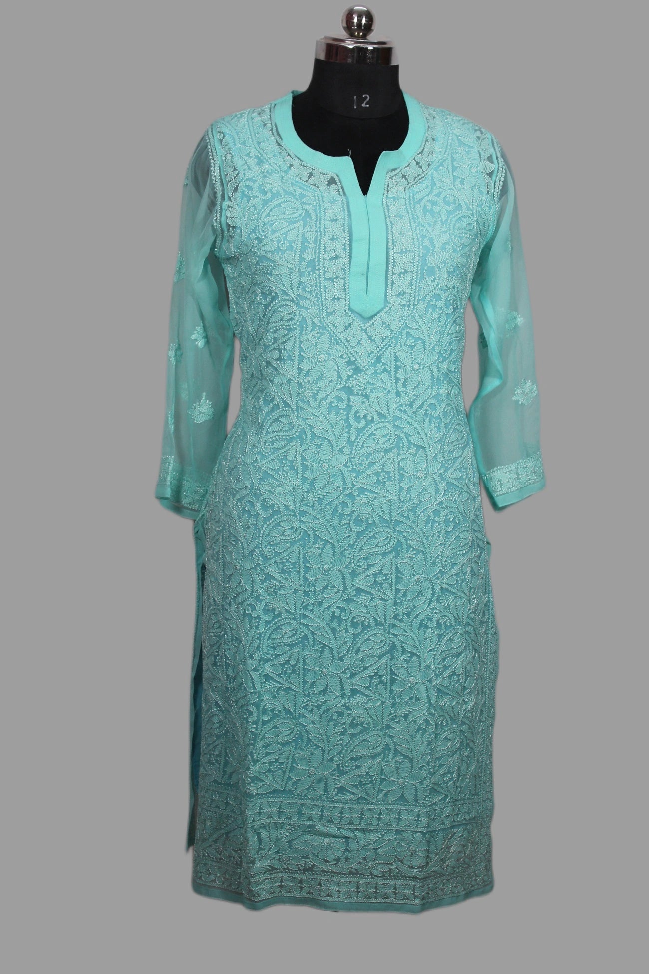 Turquoise embroidered dress on a mannequin against a gray background