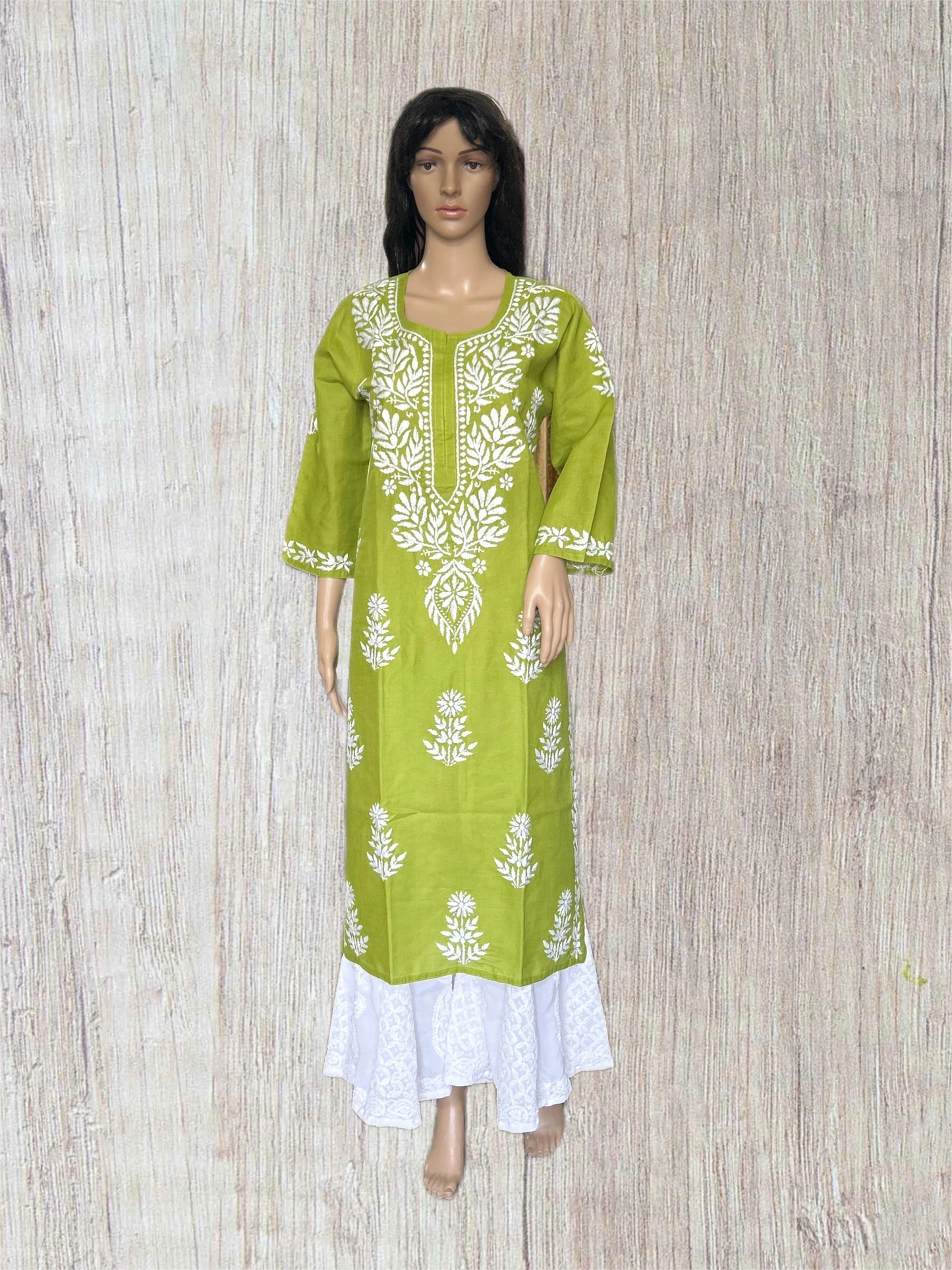 Green and white embroidered dress on a mannequin against a wooden background