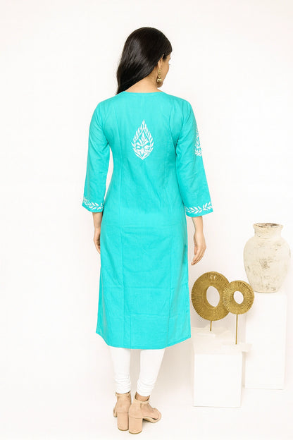Lucknowi chikankari A woman viewed from the back wearing a turquoise long kurta with white printed motifs on the back and sleeve cuffs, paired with white leggings and beige heels, standing against a white studio background with decorative vases.
