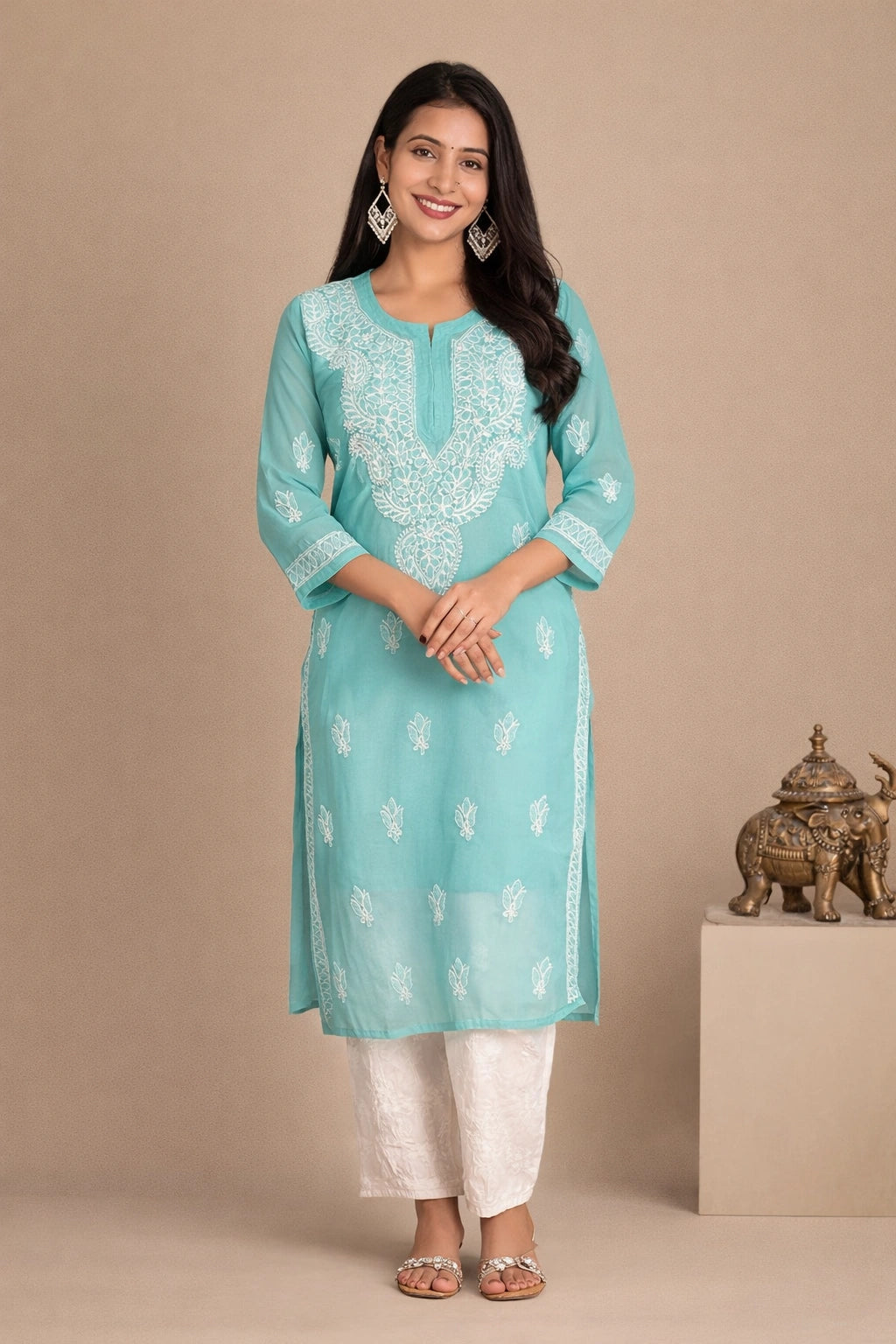 Lucknowi chikankari A woman modeling a light turquoise blue kurta with white embroidery, paired with white pants, standing against a beige studio backdrop.