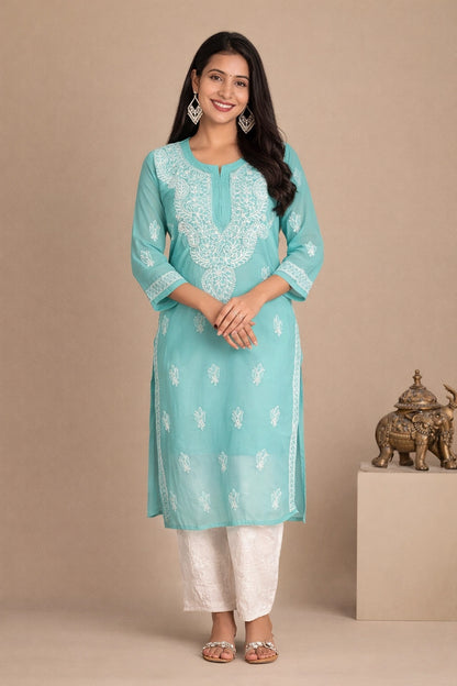 Lucknowi chikankari A woman modeling a light turquoise blue kurta with white embroidery, paired with white pants, standing against a beige studio backdrop.
