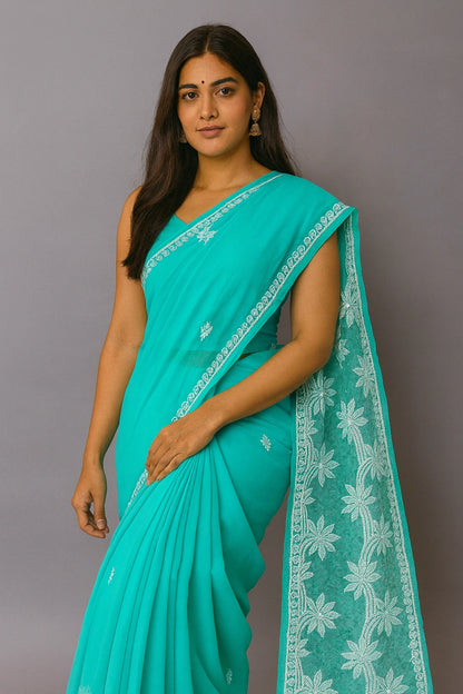 Woman wearing a lucknowi chikankari teal saree with white floral patterns on a gray background