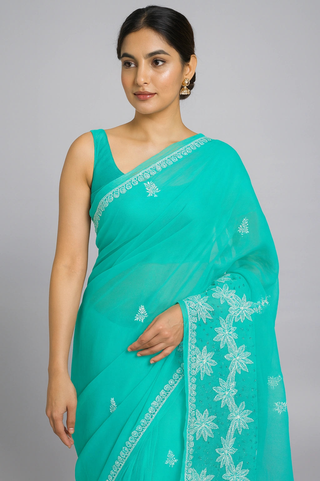 Woman wearing a teal saree with white floral embroidery on a gray background