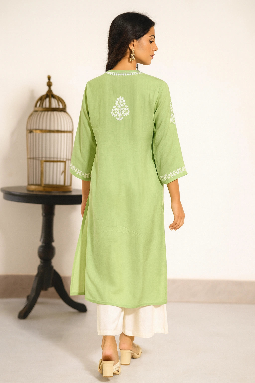 Woman wearing a light green kurta with white embroidery, standing in a minimalistic room.