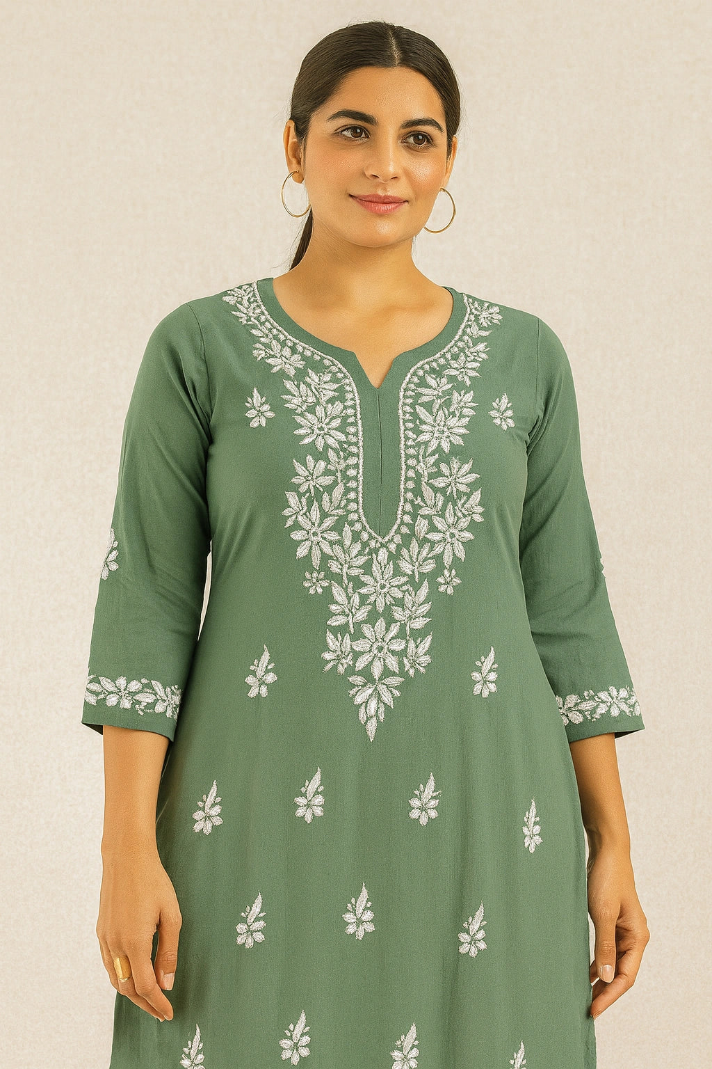 Woman wearing a green embroidered dress against a beige background