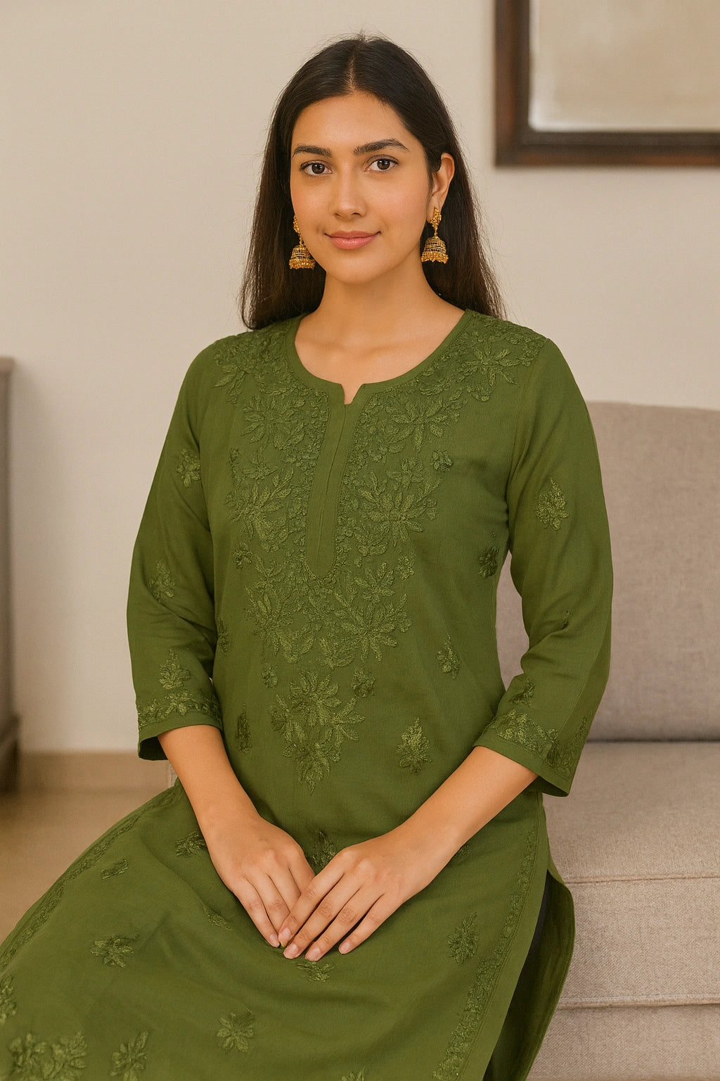 Woman wearing a green embroidered dress sitting on a couch.