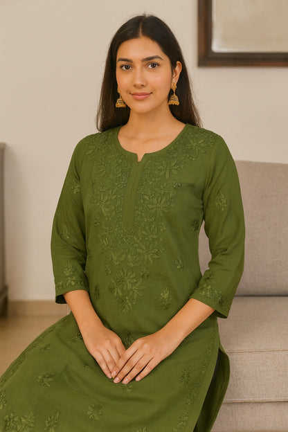 Woman wearing a green embroidered dress sitting on a couch.