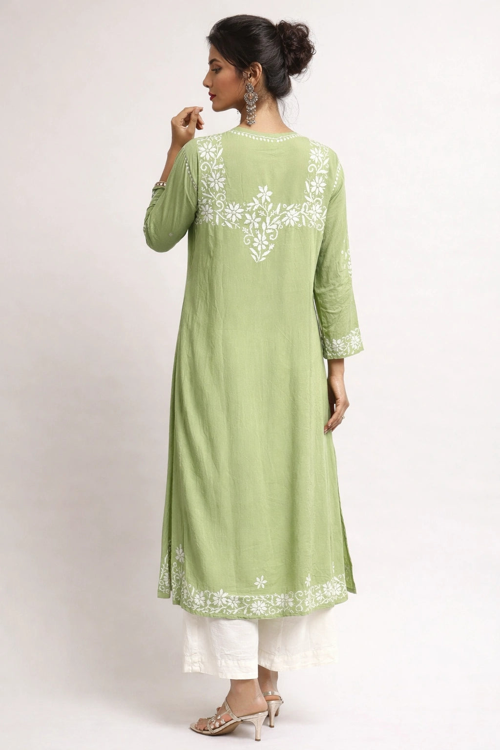 Woman wearing a green embroidered dress against a beige background