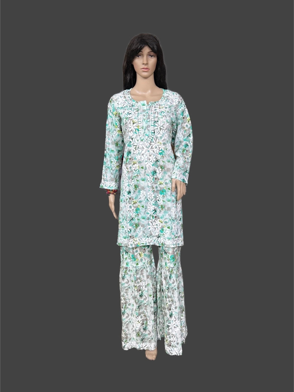 Lucknowi chikankari A mannequin wearing a long-sleeve kurta and matching wide-leg pants set with a white base and green floral pattern, shown against a dark gray background.
