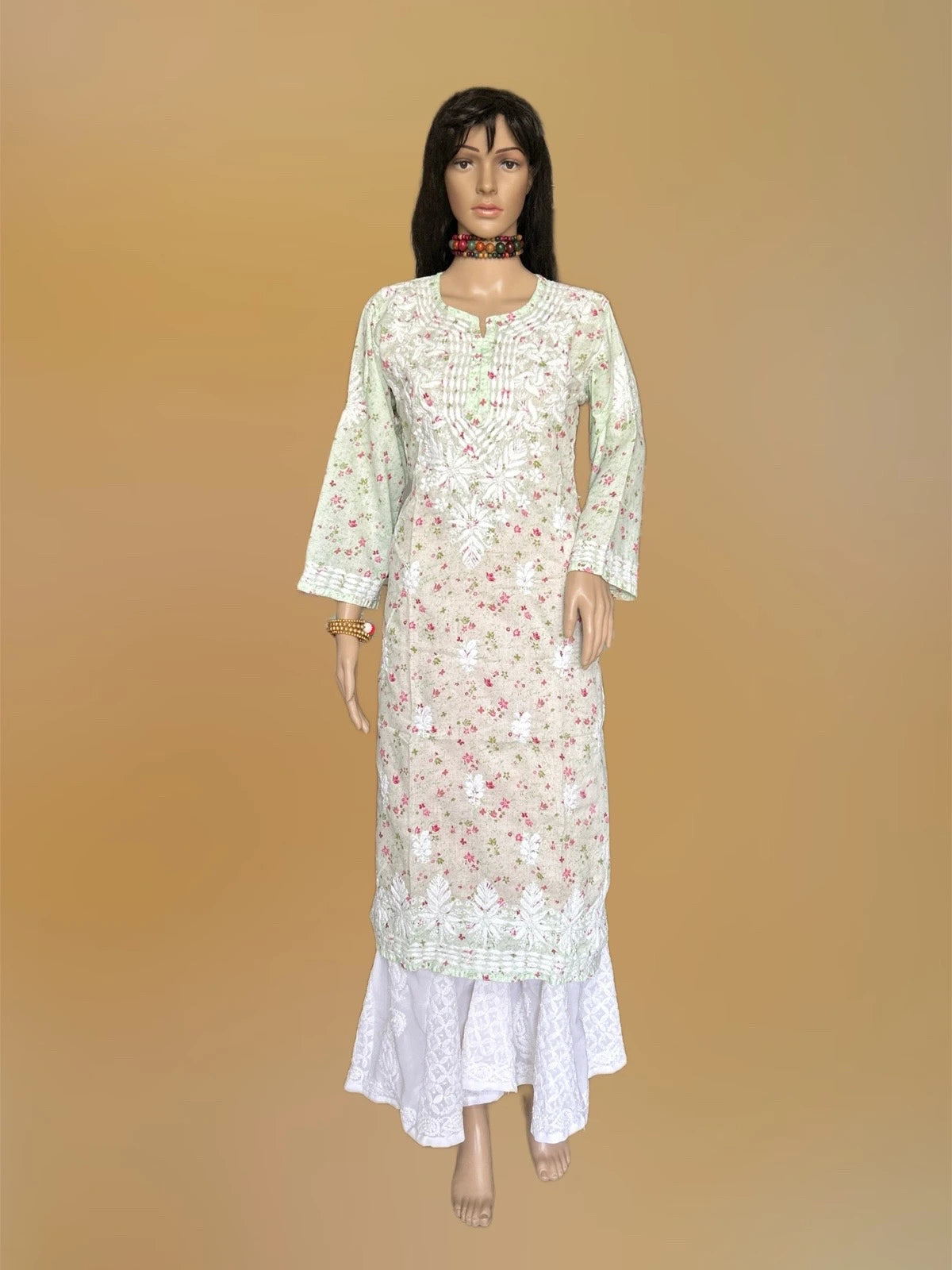 A long white embroidered kurta with pink floral patterns and green border detailing, displayed on a female mannequin against a solid tan background.