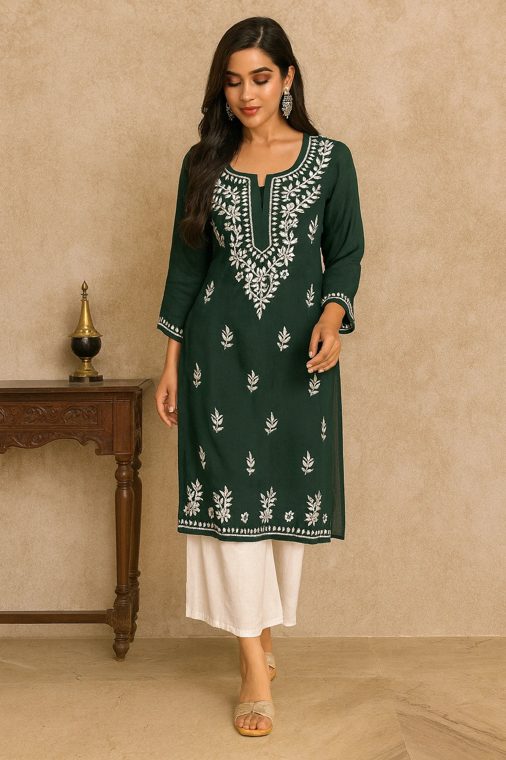 Woman wearing a green embroidered kurta with white pants against a beige wall.