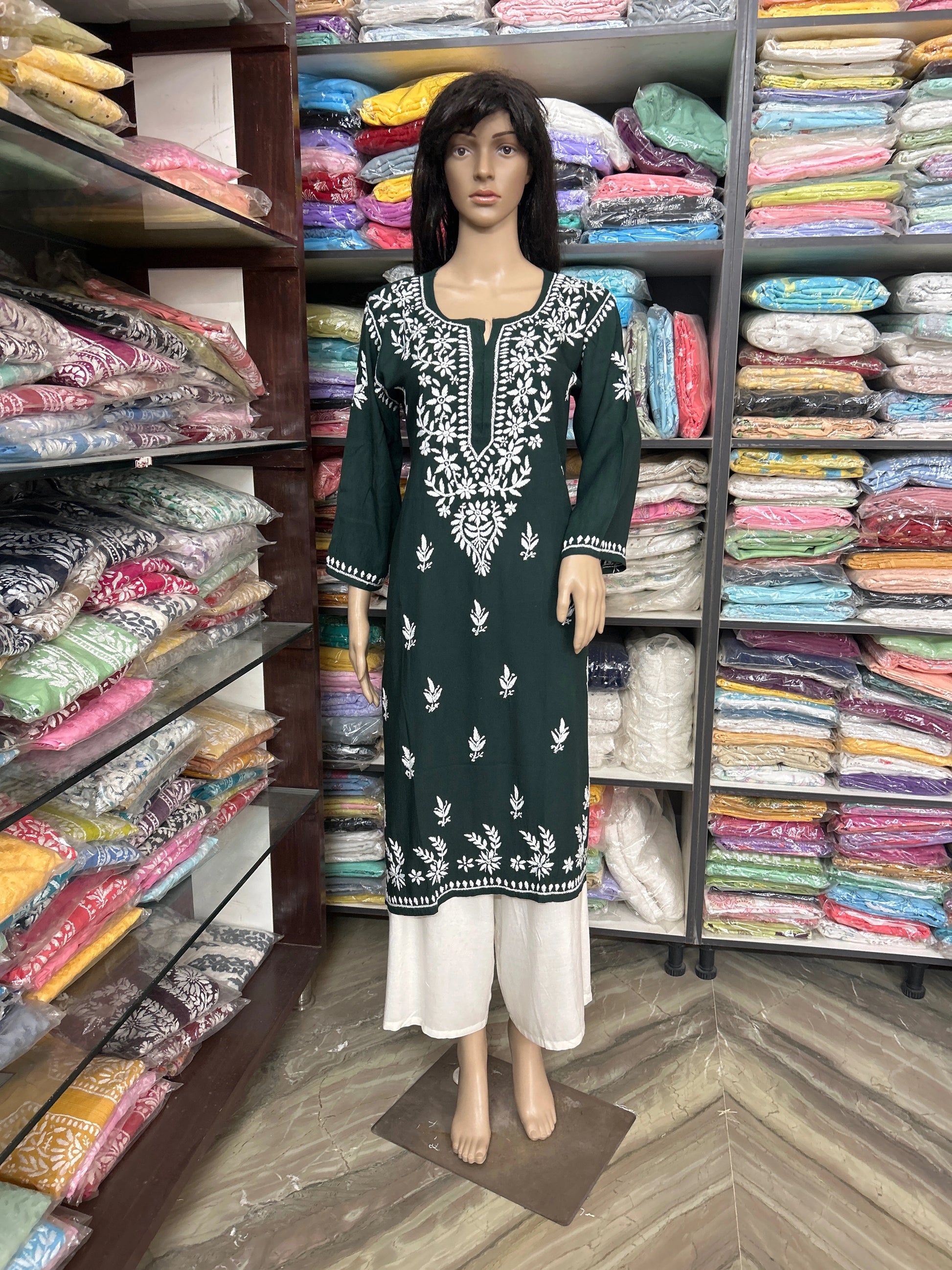 Mannequin wearing a green and white embroidered dress in a fabric store.