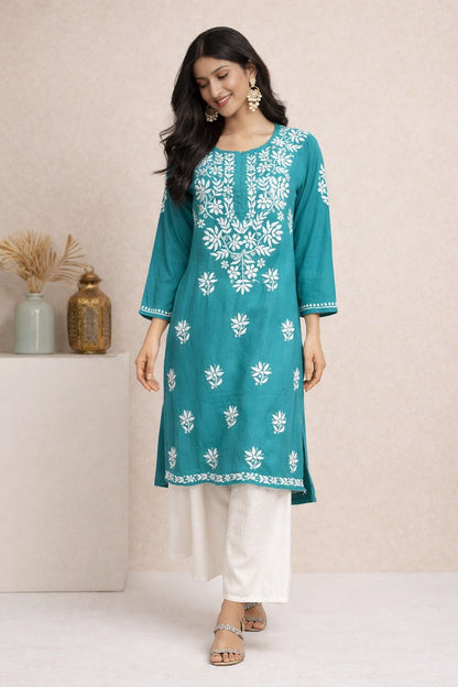Woman wearing a teal embroidered kurta with white pants against a neutral background