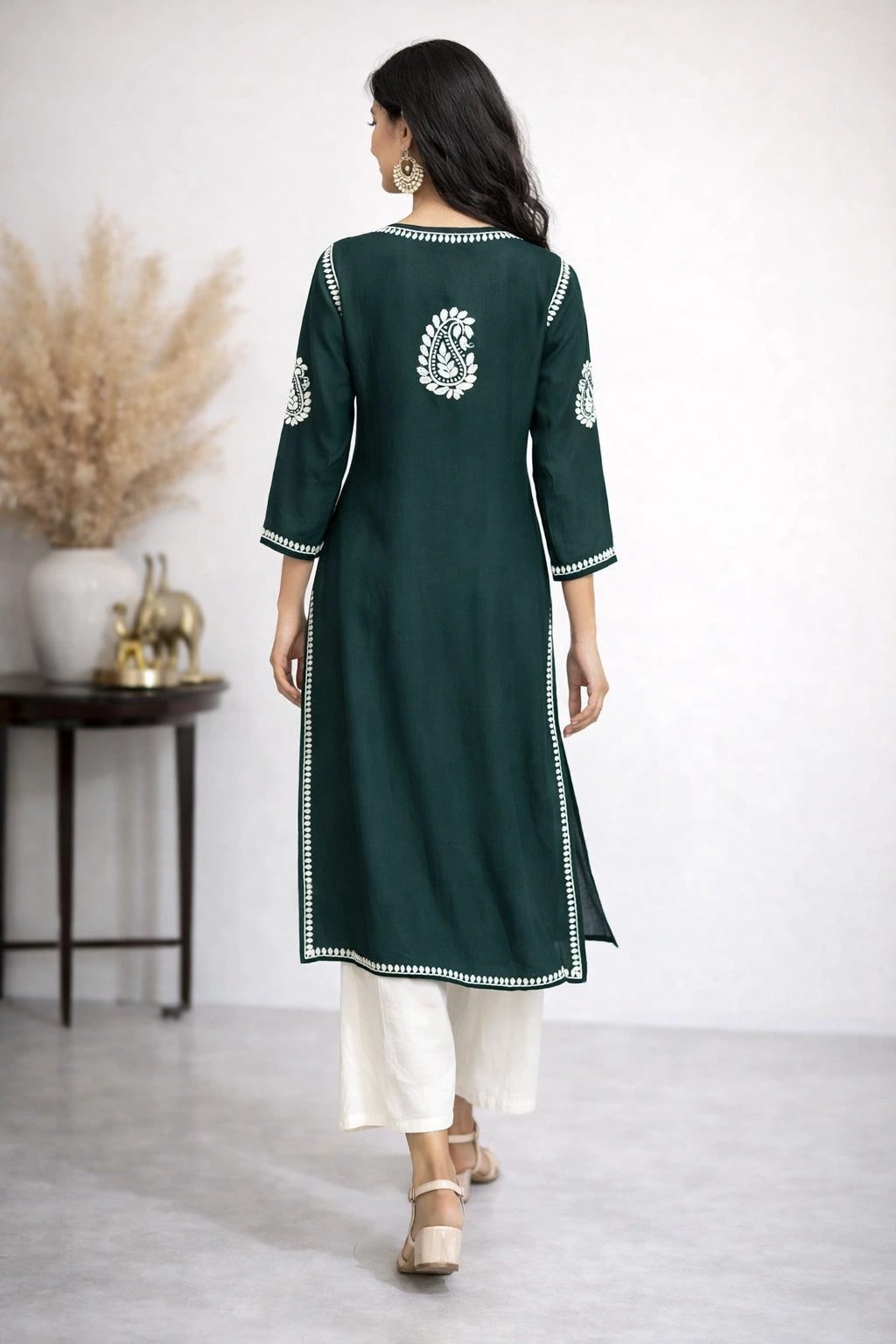 Woman wearing a green embroidered kurta with white pants in a minimalistic setting.