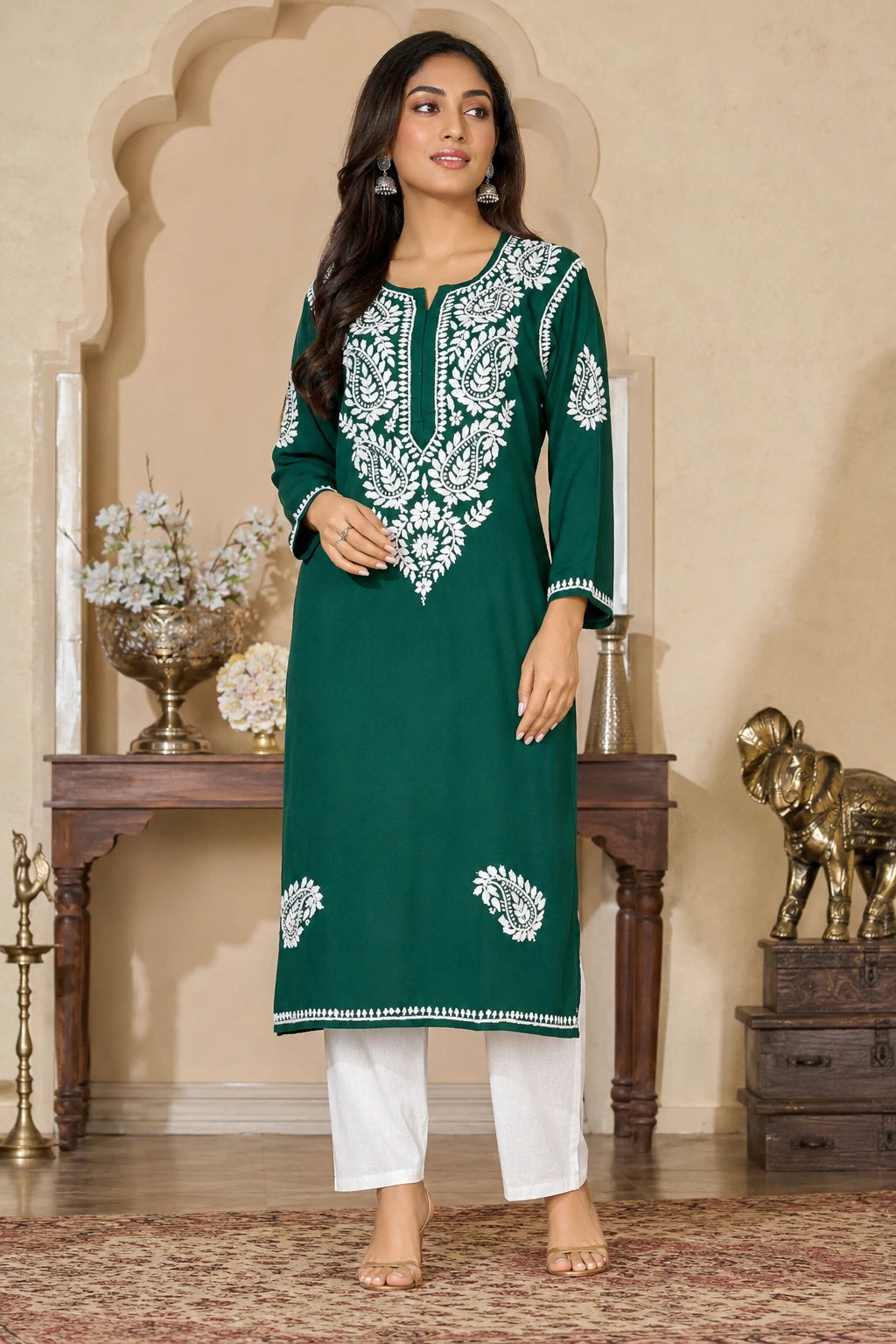 Woman wearing a green embroidered kurta with white pants in an ornate room.