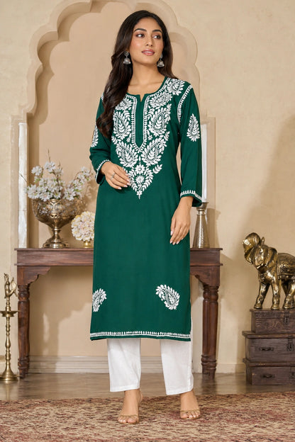Woman wearing a green embroidered kurta with white pants in an ornate room.