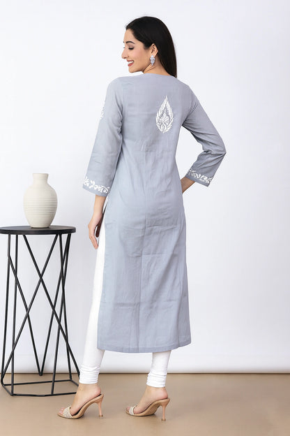 A woman modeling a light gray three-quarter sleeve kurta with white floral embroidery, paired with white pants and beige heels, shown from the back against a neutral beige background.