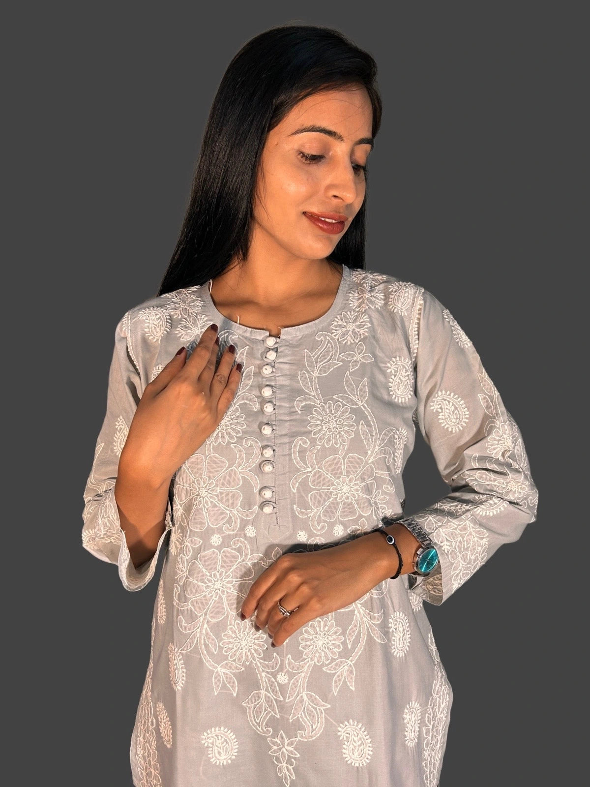 A woman wearing a light gray long-sleeve kurta with white floral embroidery and a buttoned neckline, posed against a solid dark gray background.