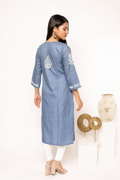 A woman modeling a light gray three-quarter sleeve kurta with white floral embroidery, paired with white pants and beige heels, shown from the back against a neutral beige background.