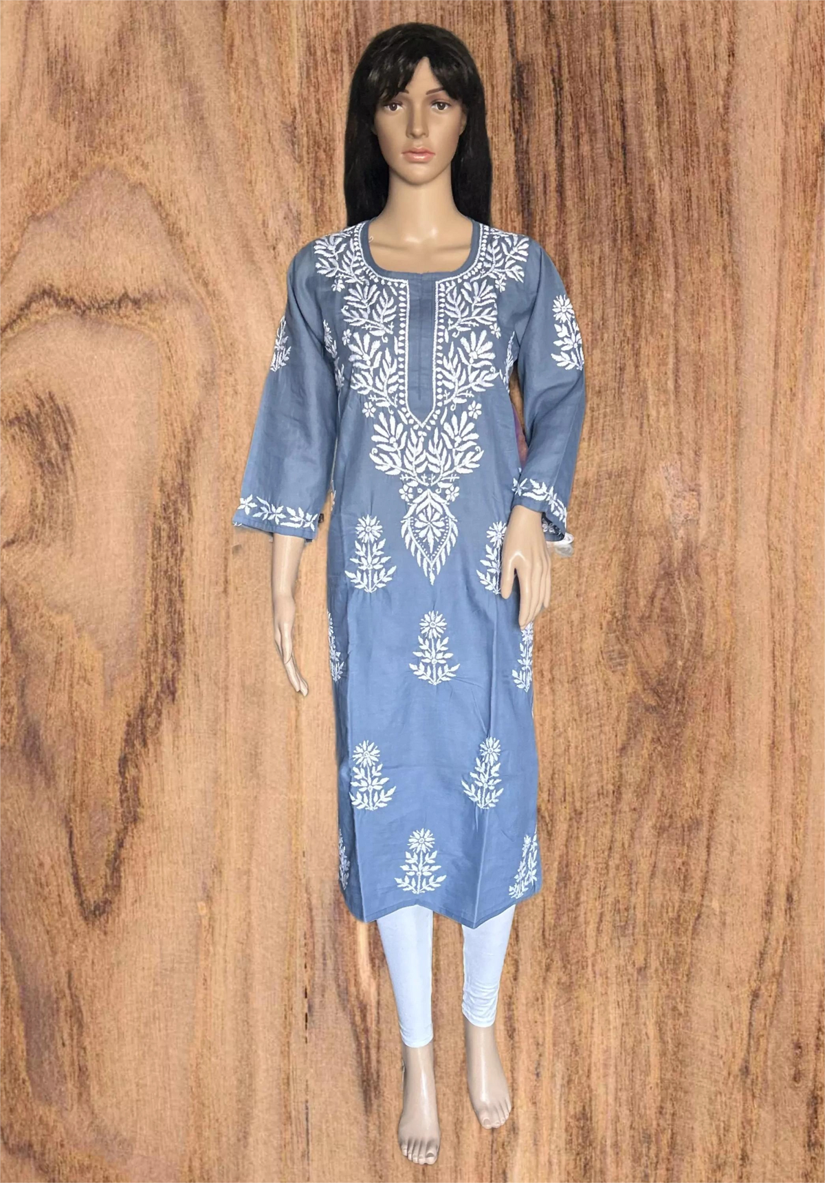 A woman wearing a light gray long-sleeve kurta with white floral embroidery and a buttoned neckline, posed against a solid dark gray background.