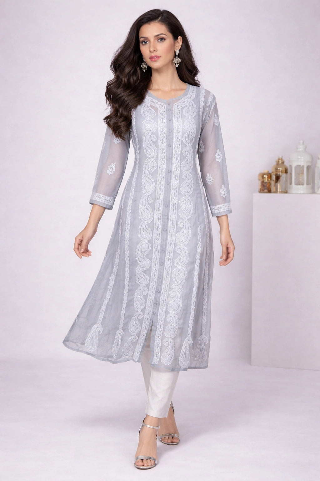 Woman wearing a embroidered light gray traditional outfit with white patterns on a white background