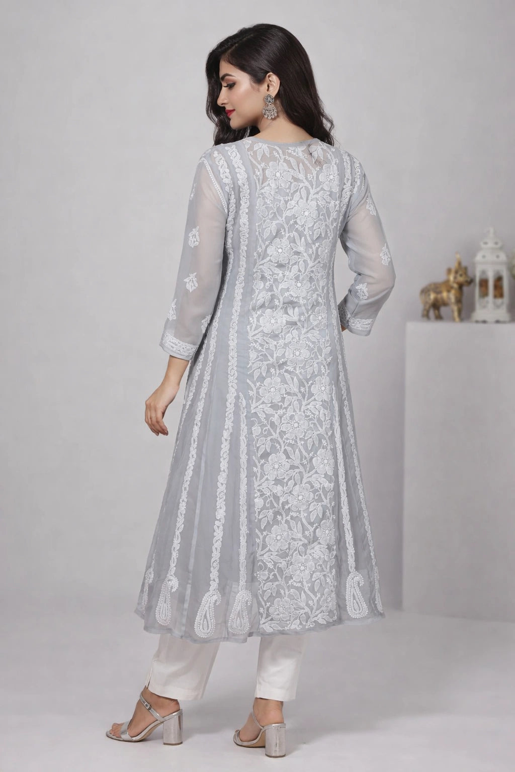 Woman wearing a light gray embroidered anarkali suit on a plain background