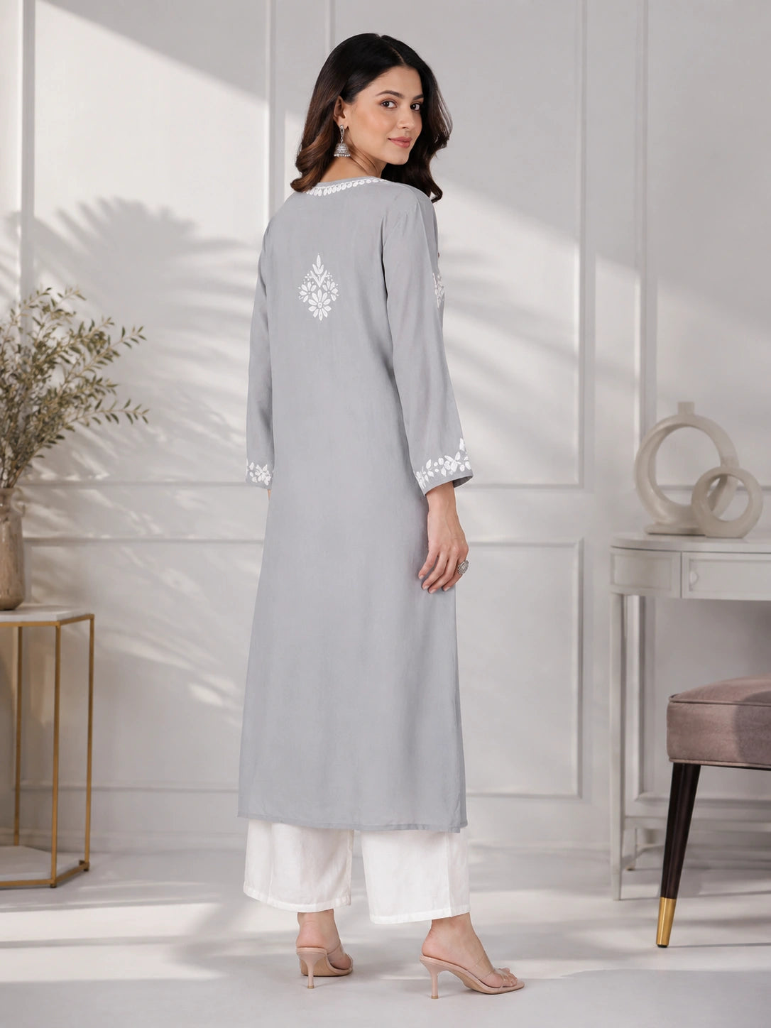 Woman wearing a grey embroidered dress against a beige background