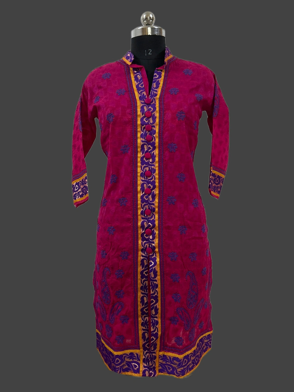 A magenta pink embroidered kurta displayed on a black dress form mannequin against a dark gray background. The kurta features purple floral embroidery and gold borders along the front placket, cuffs, and hem.