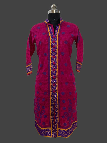 A magenta pink embroidered kurta displayed on a black dress form mannequin against a dark gray background. The kurta features purple floral embroidery and gold borders along the front placket, cuffs, and hem.