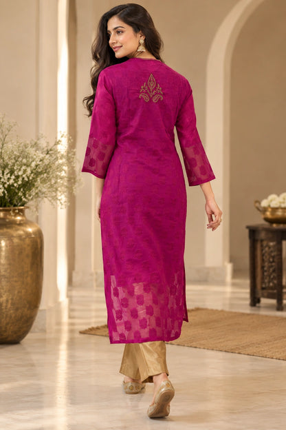 A woman wearing a magenta pink embroidered kurta with sheer sleeves and a checkered pattern near the hem, paired with beige trousers, shown from the back in an elegant indoor setting.