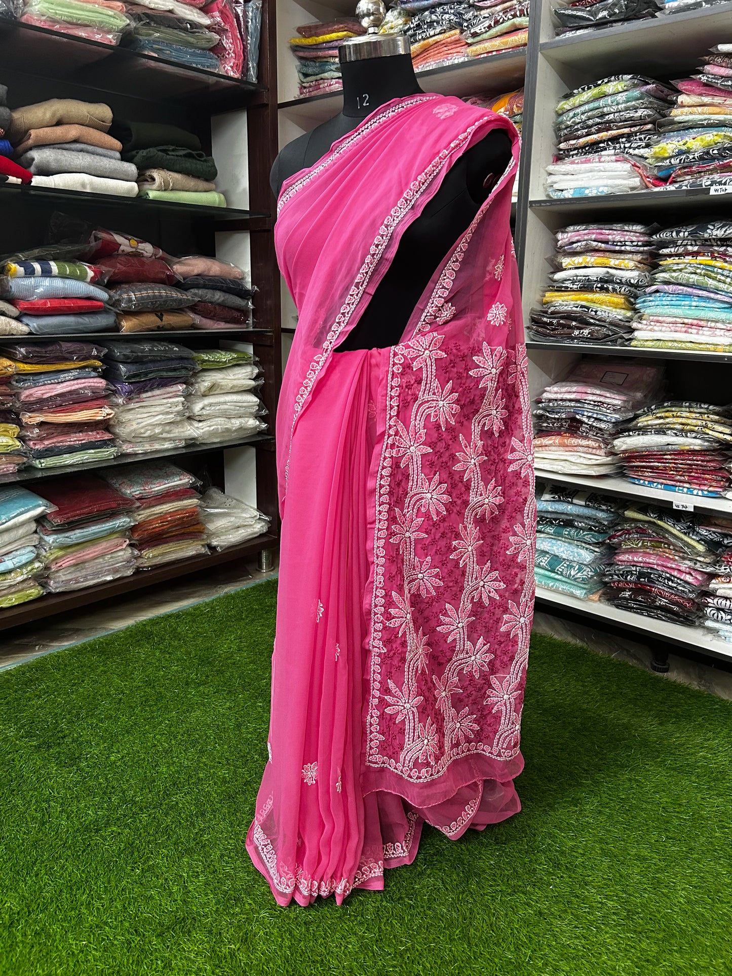 Pink saree with white embroidery on a mannequin in a fabric store.