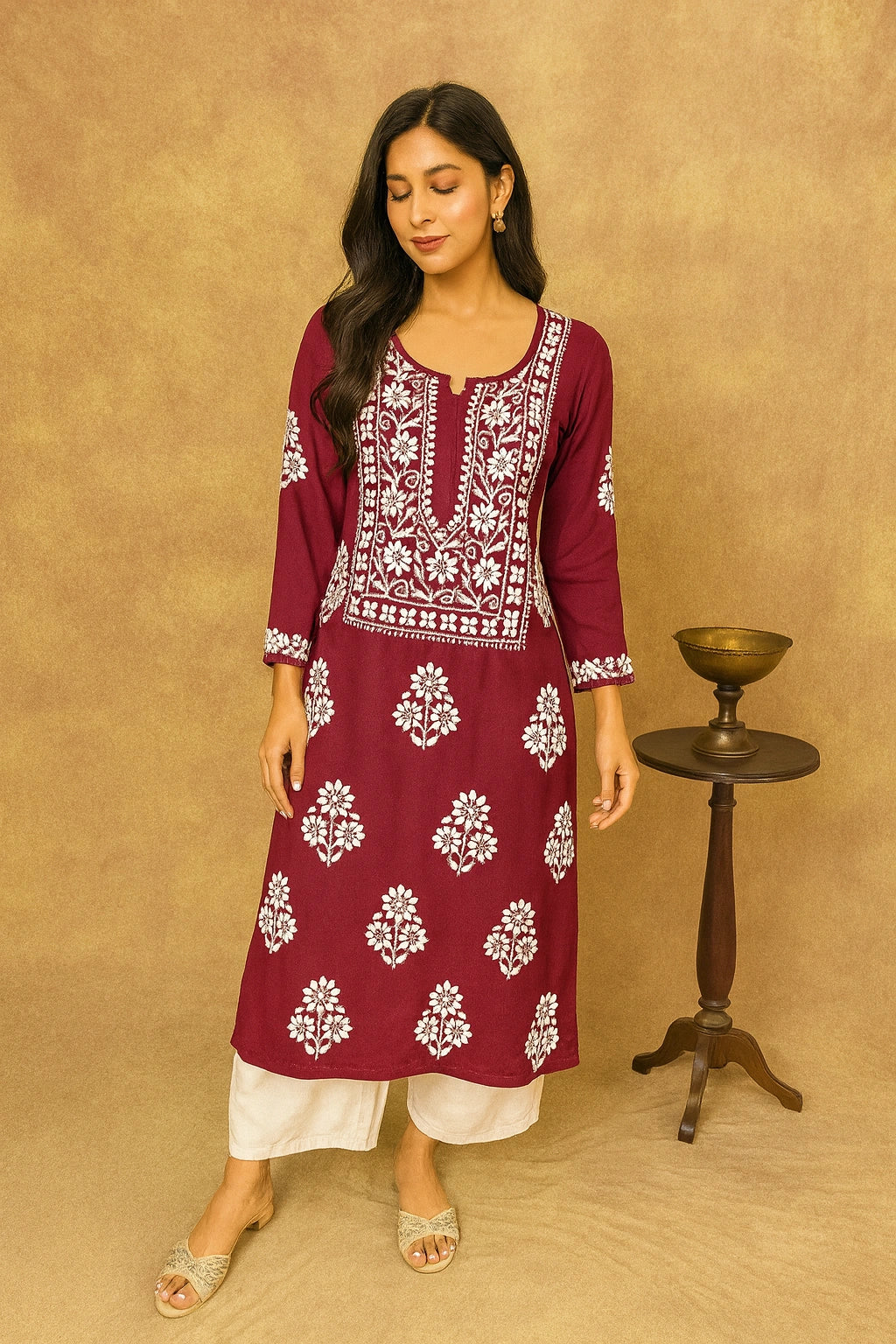 Woman wearing a maroon embroidered kurta with white pants against a beige background